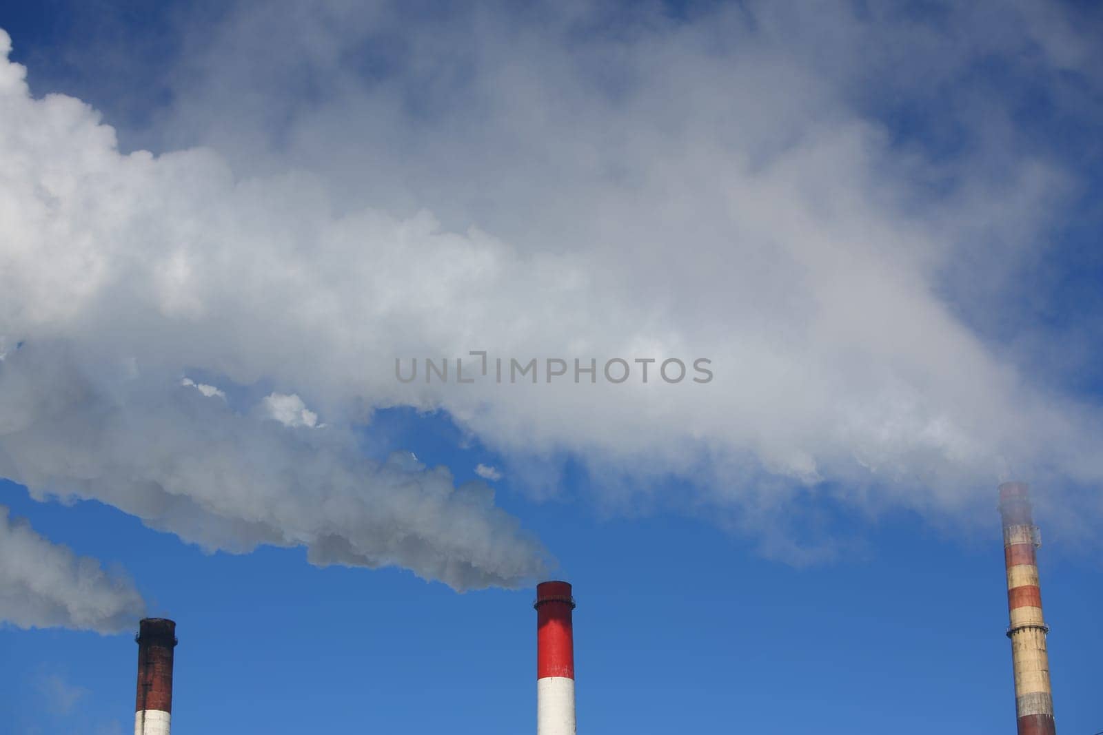 Three pipes of thermal power plant with steam and smoke against blue sky during heating season by kuprevich