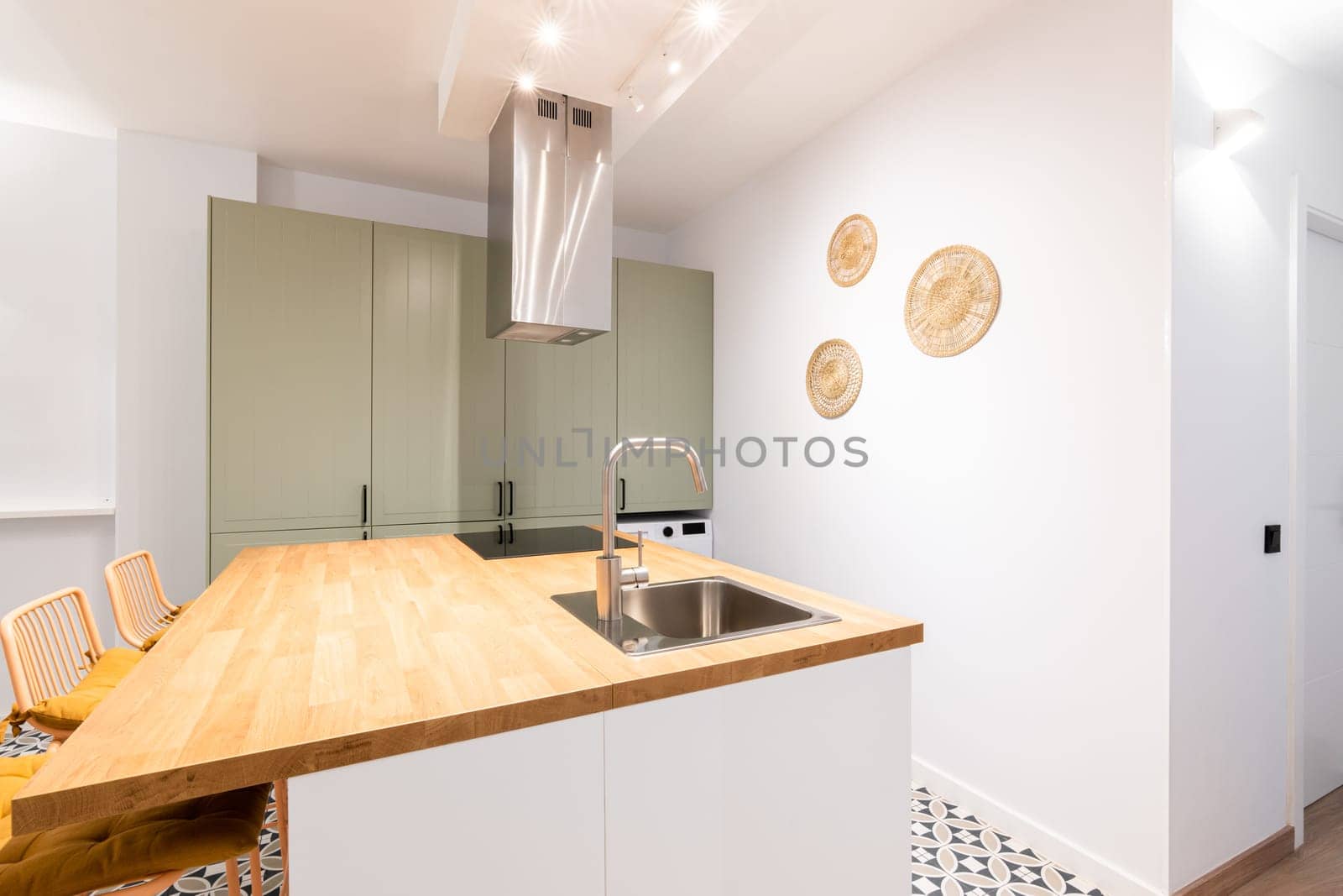 Designer kitchen with bright lighting from wall lamps. Table with sink and faucet in chromed metal. Above the electric stove, system for purifying the air from odors during cooking