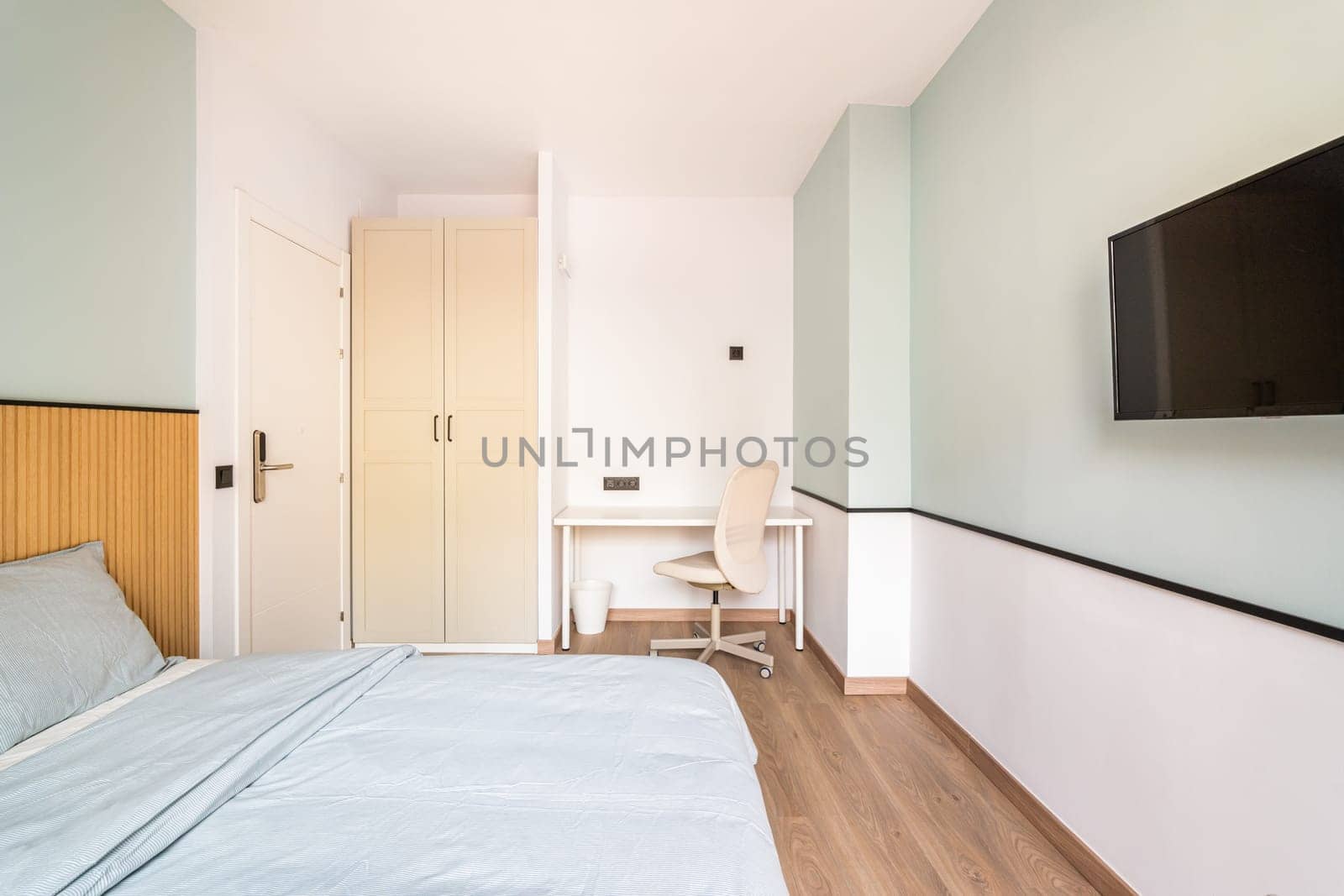 Hotel room with bed for two persons with beige linen. . Table against wall with chair for online work. On wall is TV for pleasant evenings watching movie. by apavlin