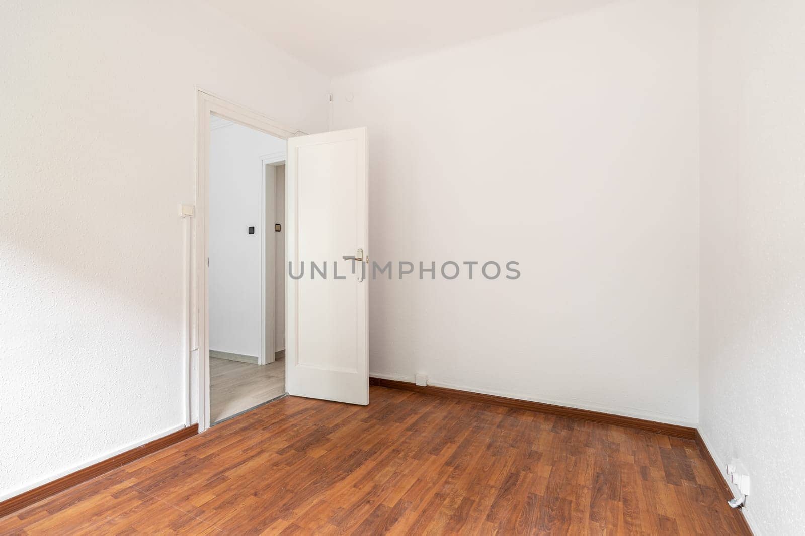 Empty spacious room well lit by daylight. The floor is dark brown wood parquet. White walls with a doorway opening onto a corridor. Through the open door you can see part of the rest of the apartment. by apavlin