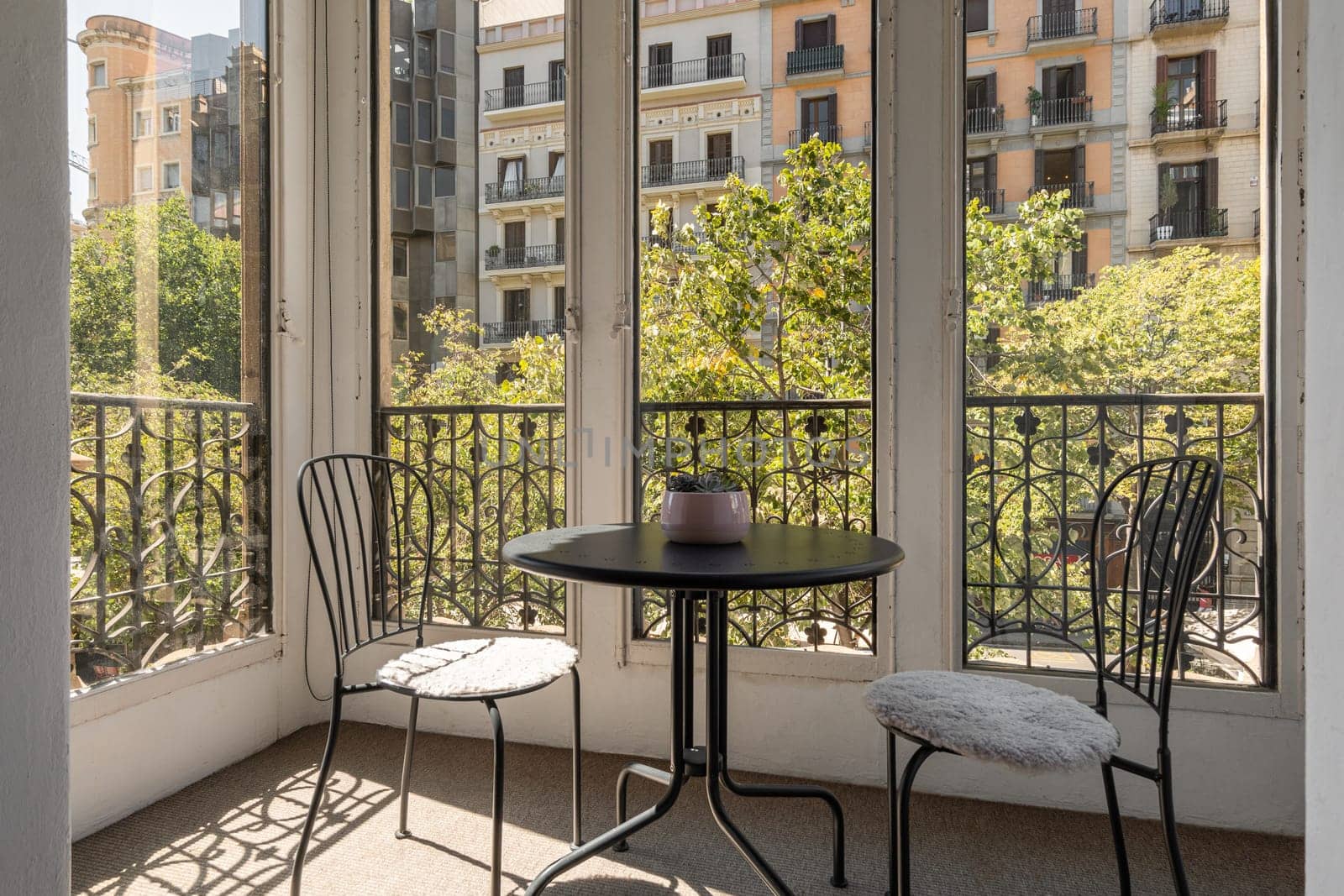 Two iron chairs and table on closed glazed terrace with beautiful view of cozy new area of warm country on sunny summer day. Concept of a romantic hotel room for honeymooners.