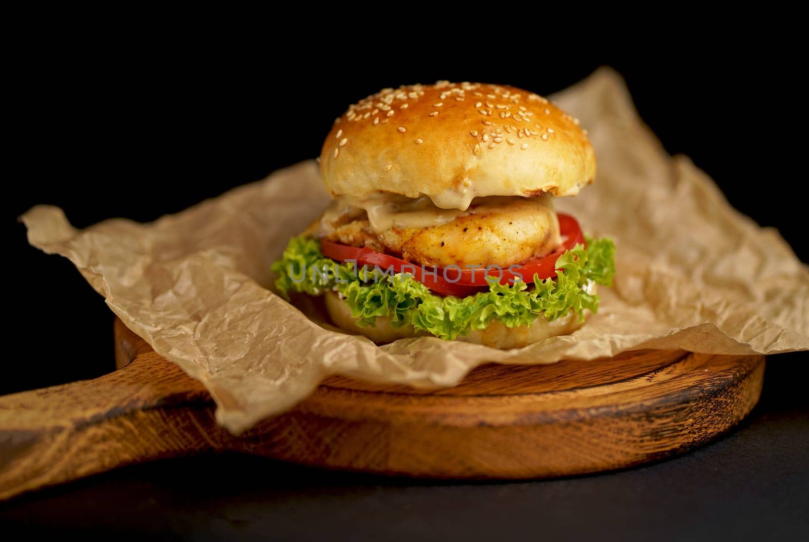 Close-up of a delicious fresh homemade burger with lettuce, cheese, onion and tomato on a rustic wooden board on a dark background by aprilphoto