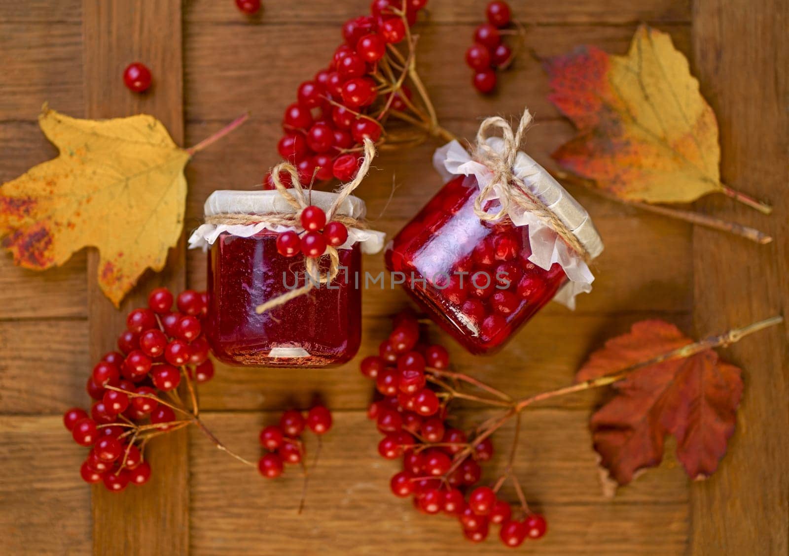Home preparations. Viburnum jam in a glass jar on a wooden table near fresh viburnum berries and autumn berries by aprilphoto