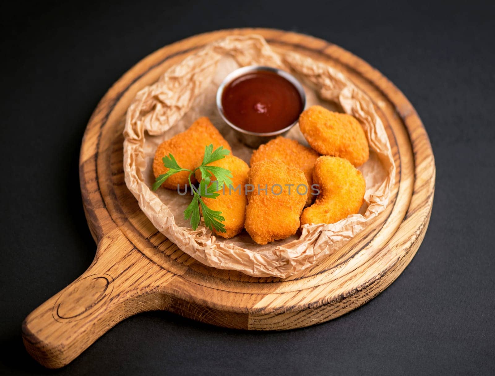 Side view of fried chicken fillet in panko breadcrumbs served with lettuce. sweet and sour sauce in saucepan near dish isolated on black background.