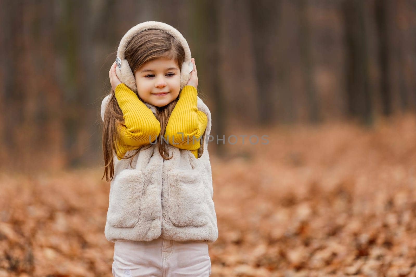 little girl in headphones walks through the autumn forest