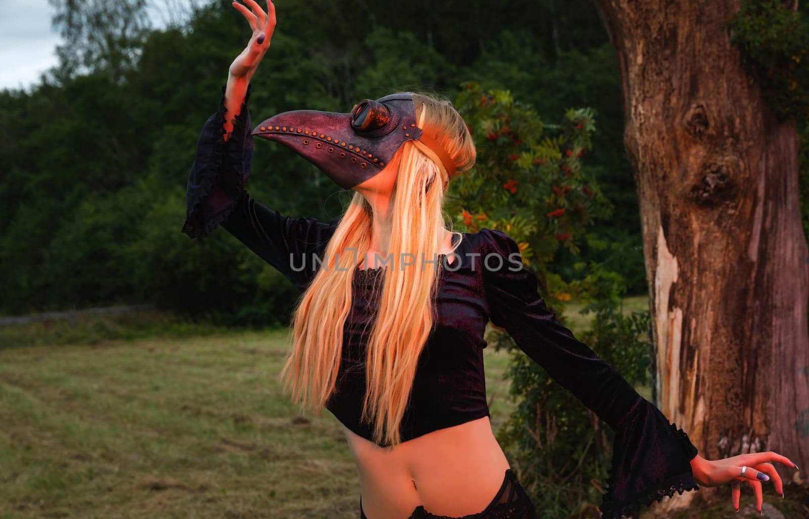 Natures beauty with a touch of mystery. A mystical and captivating image - a blonde woman in a crow mask posing near a withered tree in nature, creating an aura of mystery and beauty.