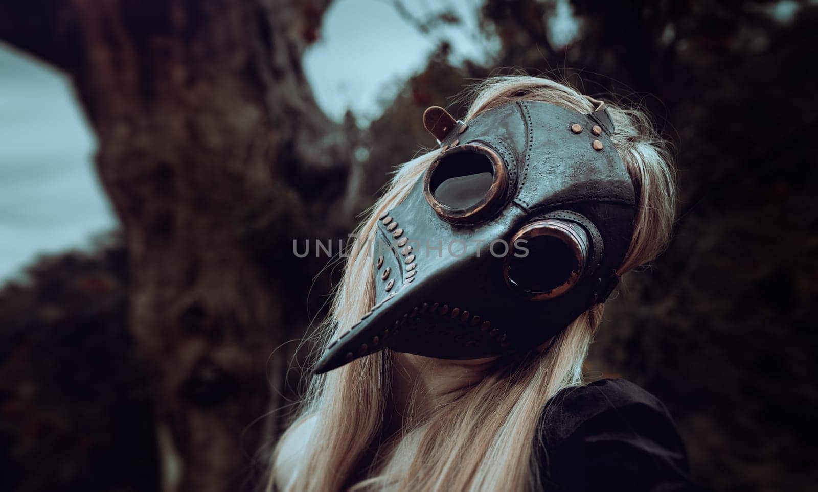 Blonde in crow mask poses in nature near old tree by palinchak