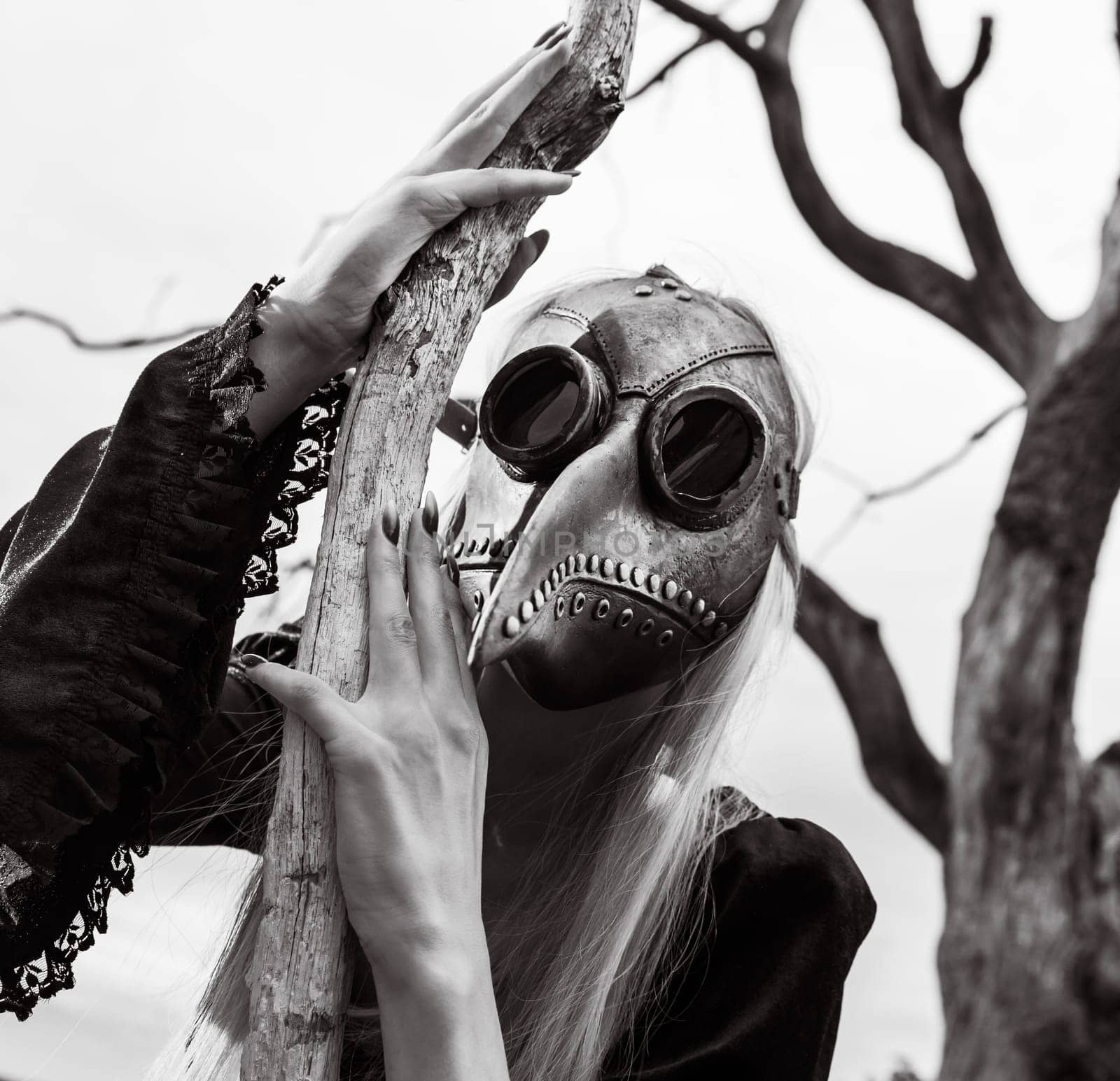 Natures beauty with a touch of mystery. A mystical and captivating image - a blonde woman in a crow mask posing near an dry tree, creating an aura of mystery and beauty. Black and white image.