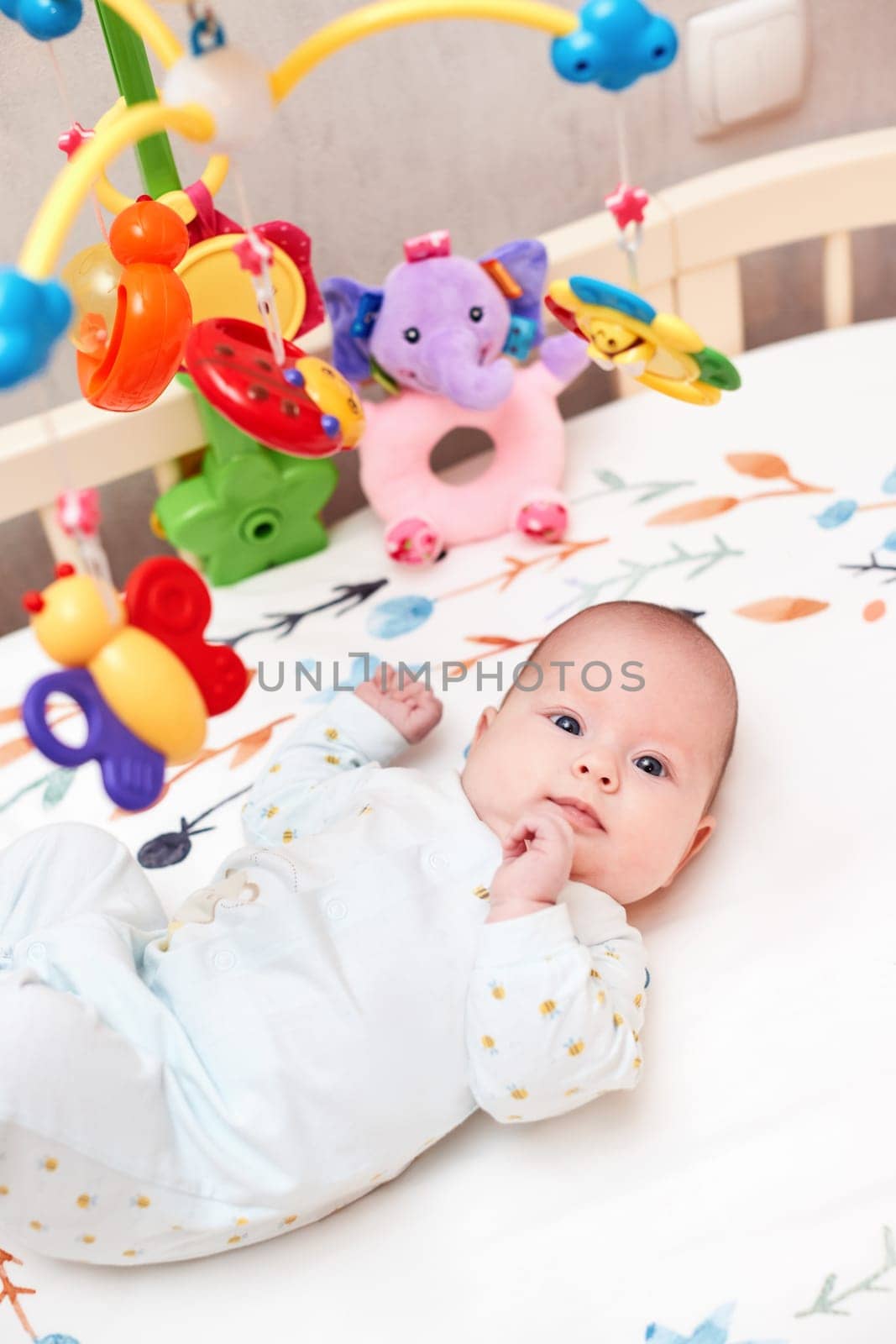 smiling cute newborn baby playing with mobile in crib at home