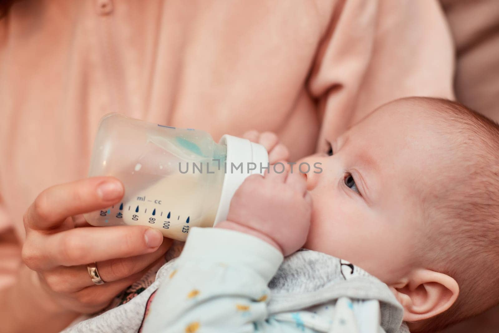 mother feeds her little cute newborn baby with milk bottle at home. Mom takes care of the child.