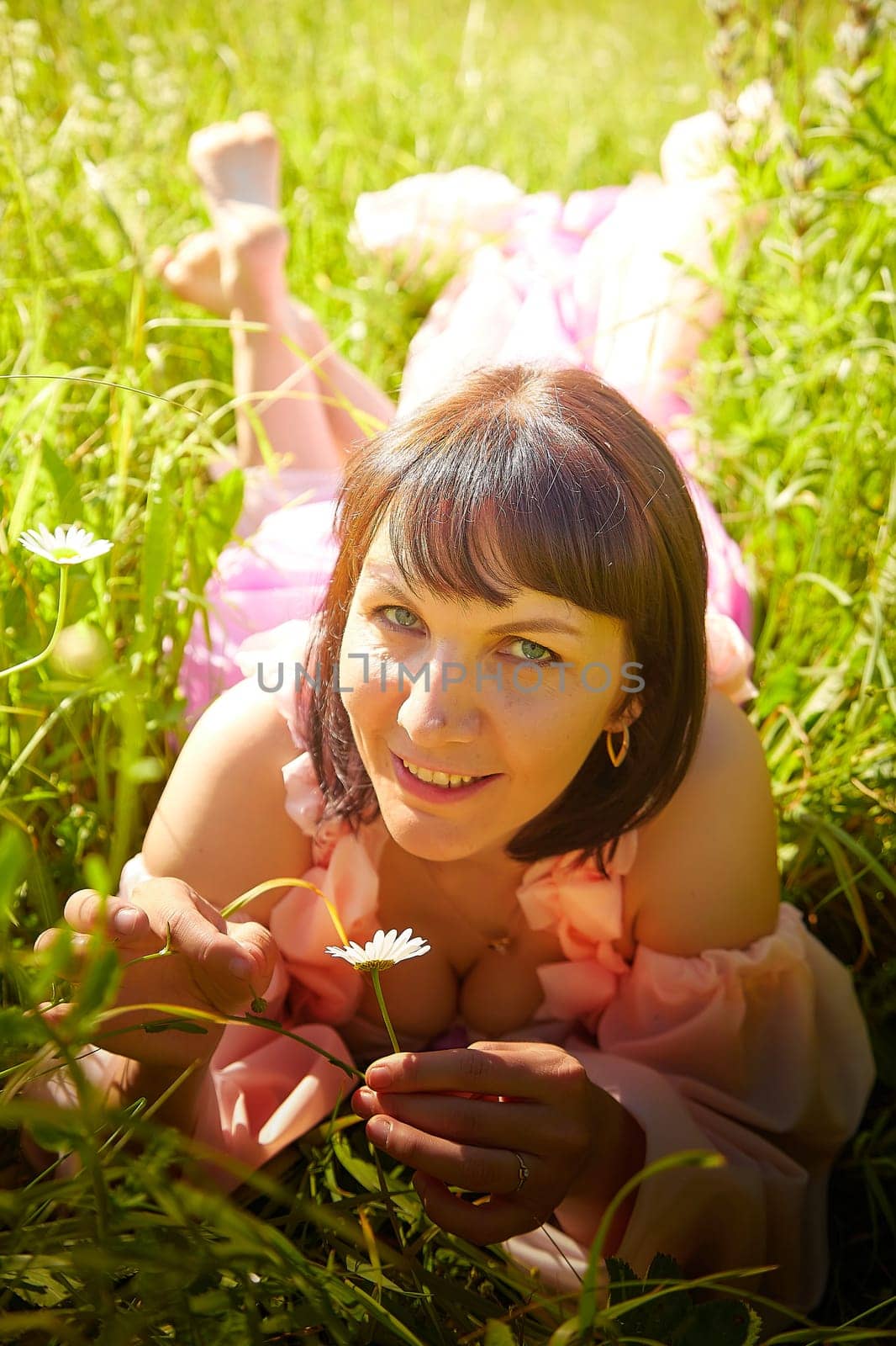 Beautiful girl in lush pink ball gown in green field during blooming of flowers and blue sky on background. Model posing on nature landscape as princess from fary tale