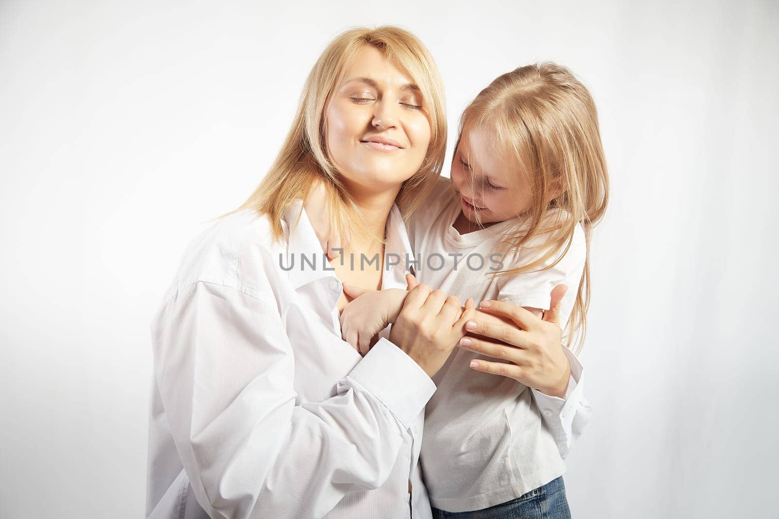 Portrait of blonde mother and daughter who having communicate and play on a white background. Mom and little girl models pose in the studio. The concept of love, friendship, caring in the family