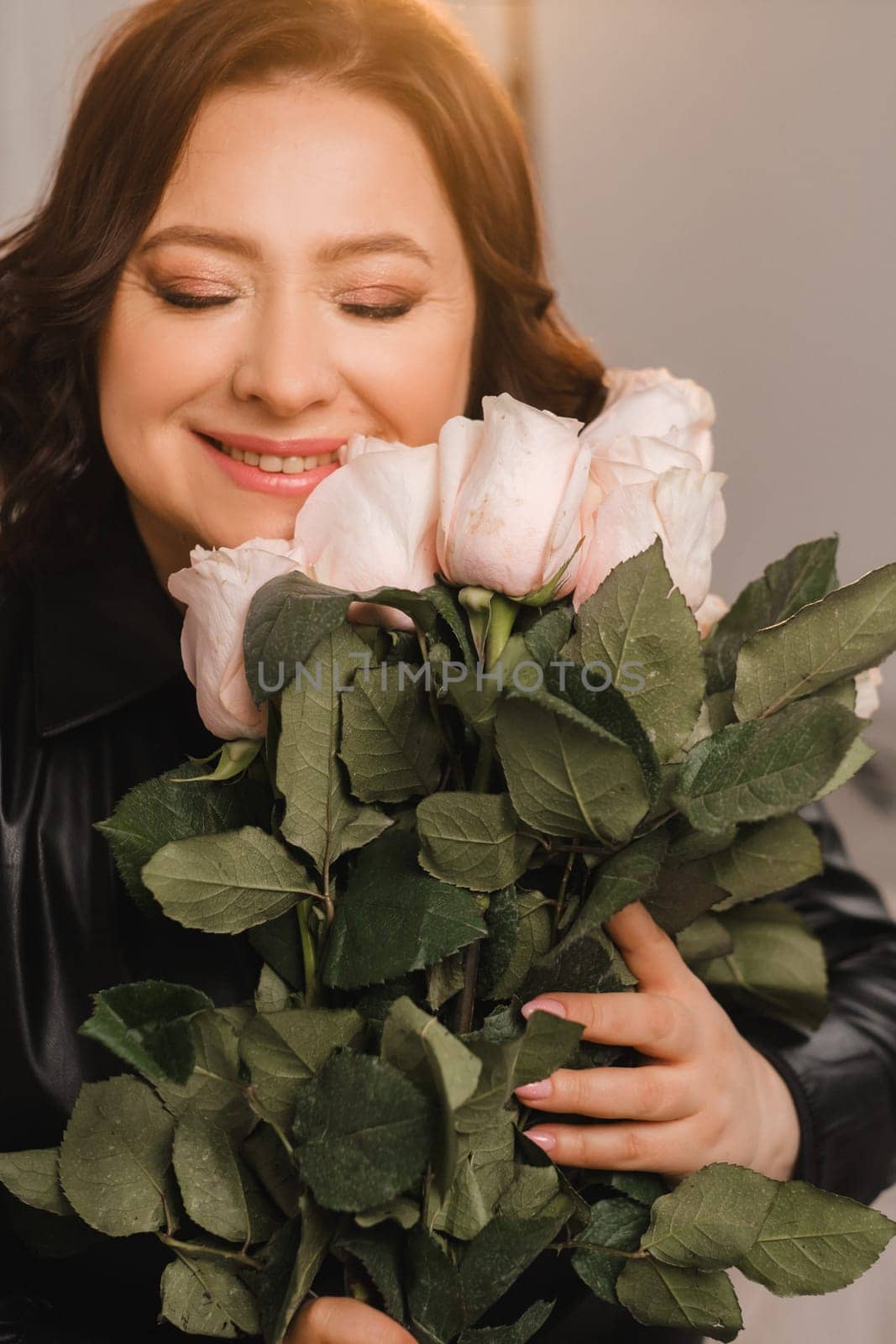 a stylish adult woman in black leather clothes stands with a bouquet of pink roses in the interior.