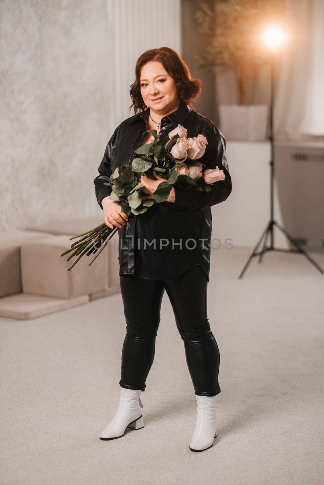 a stylish adult woman in black leather clothes stands with a bouquet of pink roses in the interior.