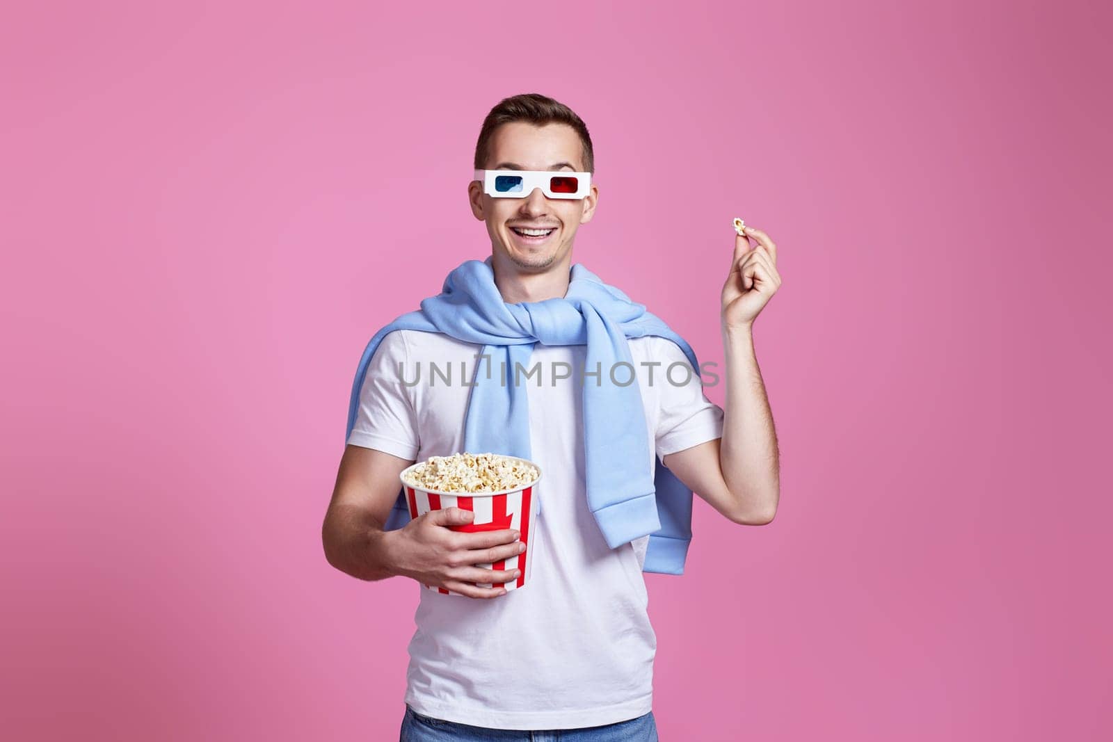 handsome man in 3d glasses, white t-shirt showing popcorn on pink background