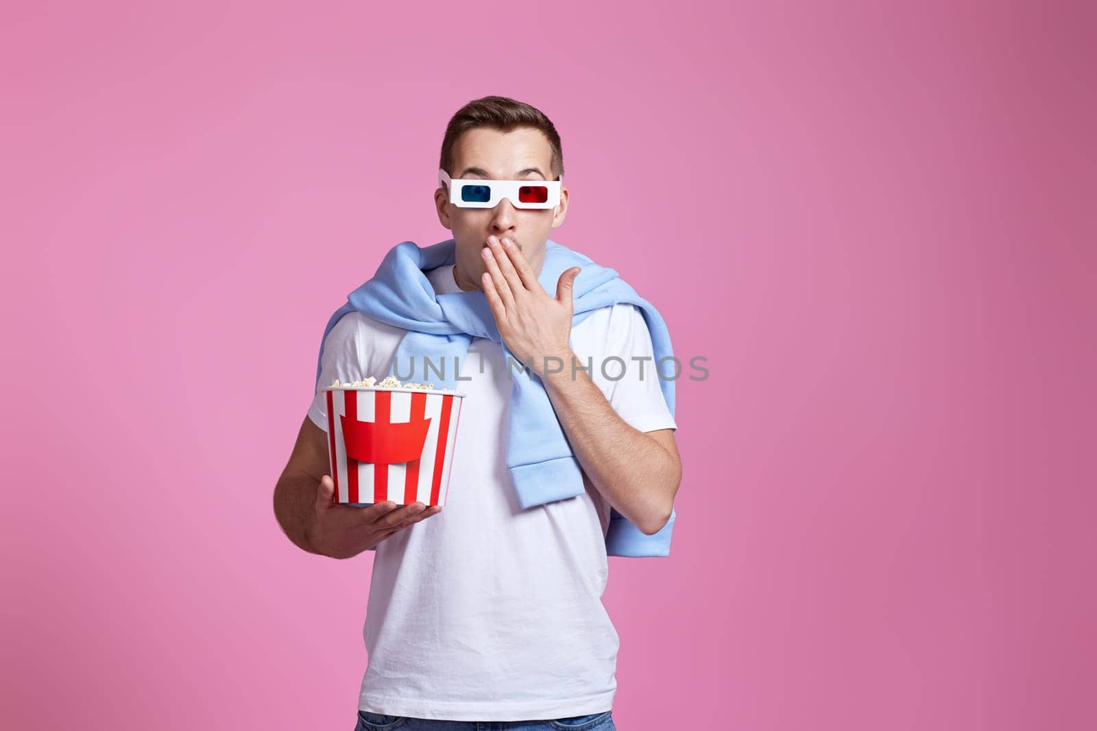 scared handsome man in 3d glasses holding bucket of popcorn on pink background