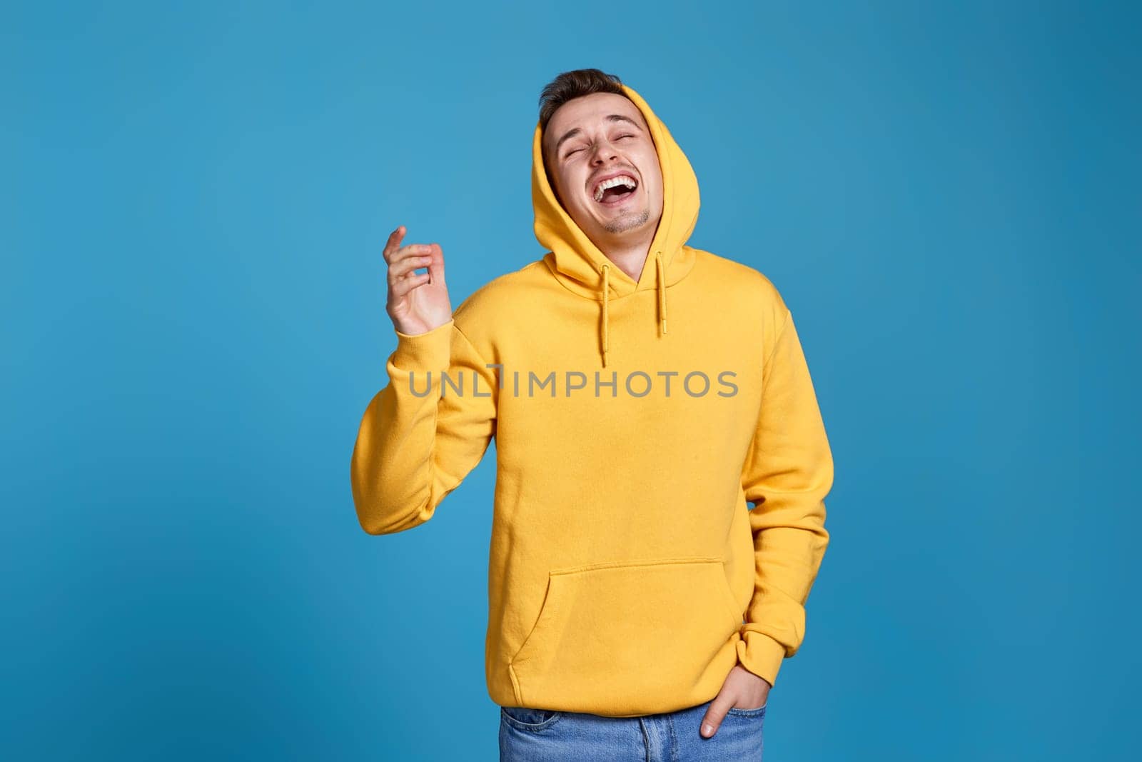 positive handsome man in yellow sweatshirt laughing on blue background