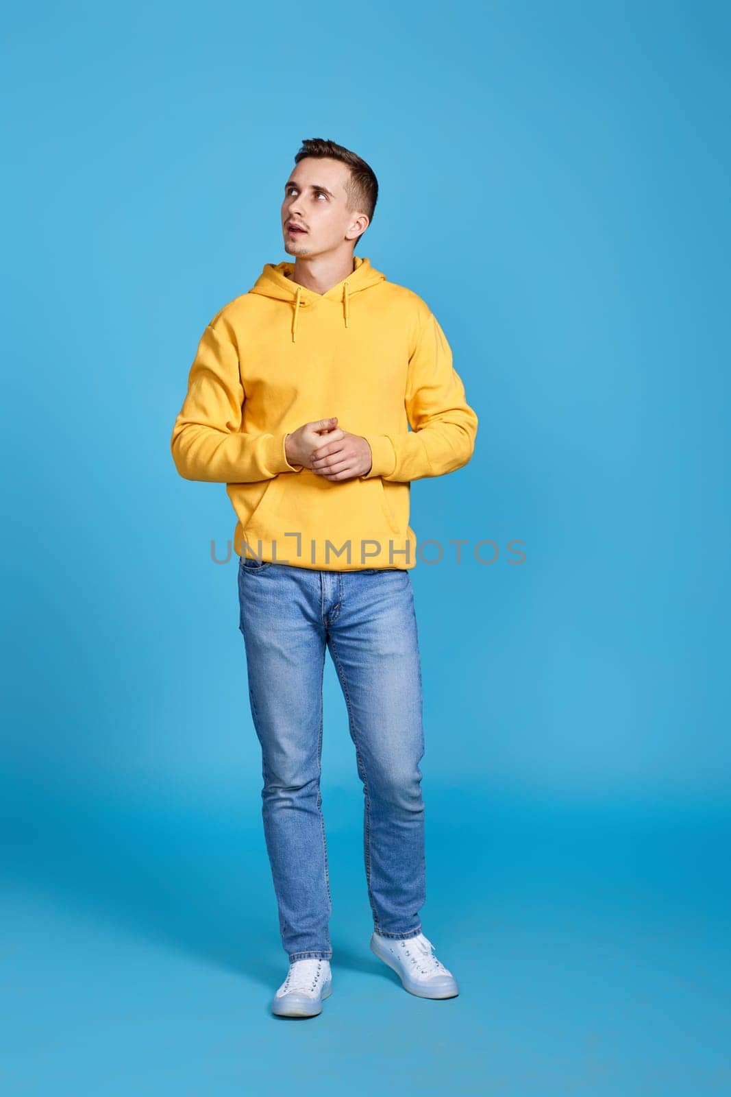 thoughtful young man thinking and looking at the side on blue background. Full length