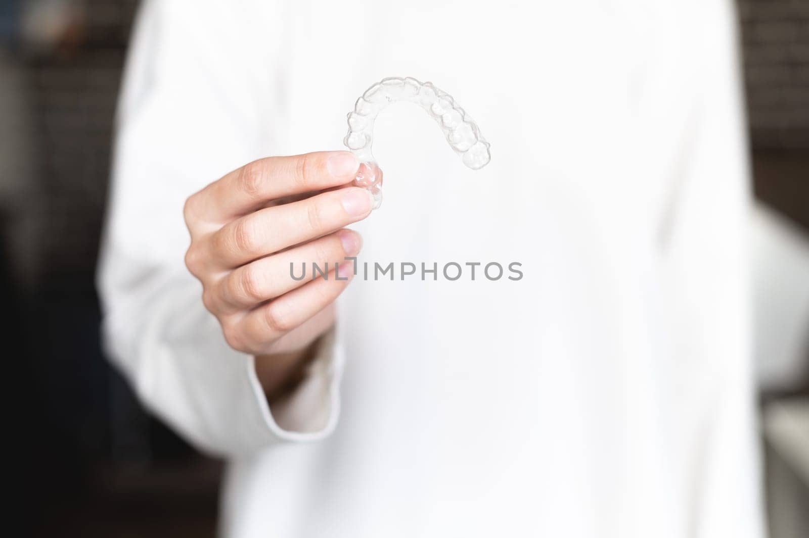 close-up of a young caucasian woman with a hand holding a dental retainer invisible. photo for beautiful teeth treatment course concept.