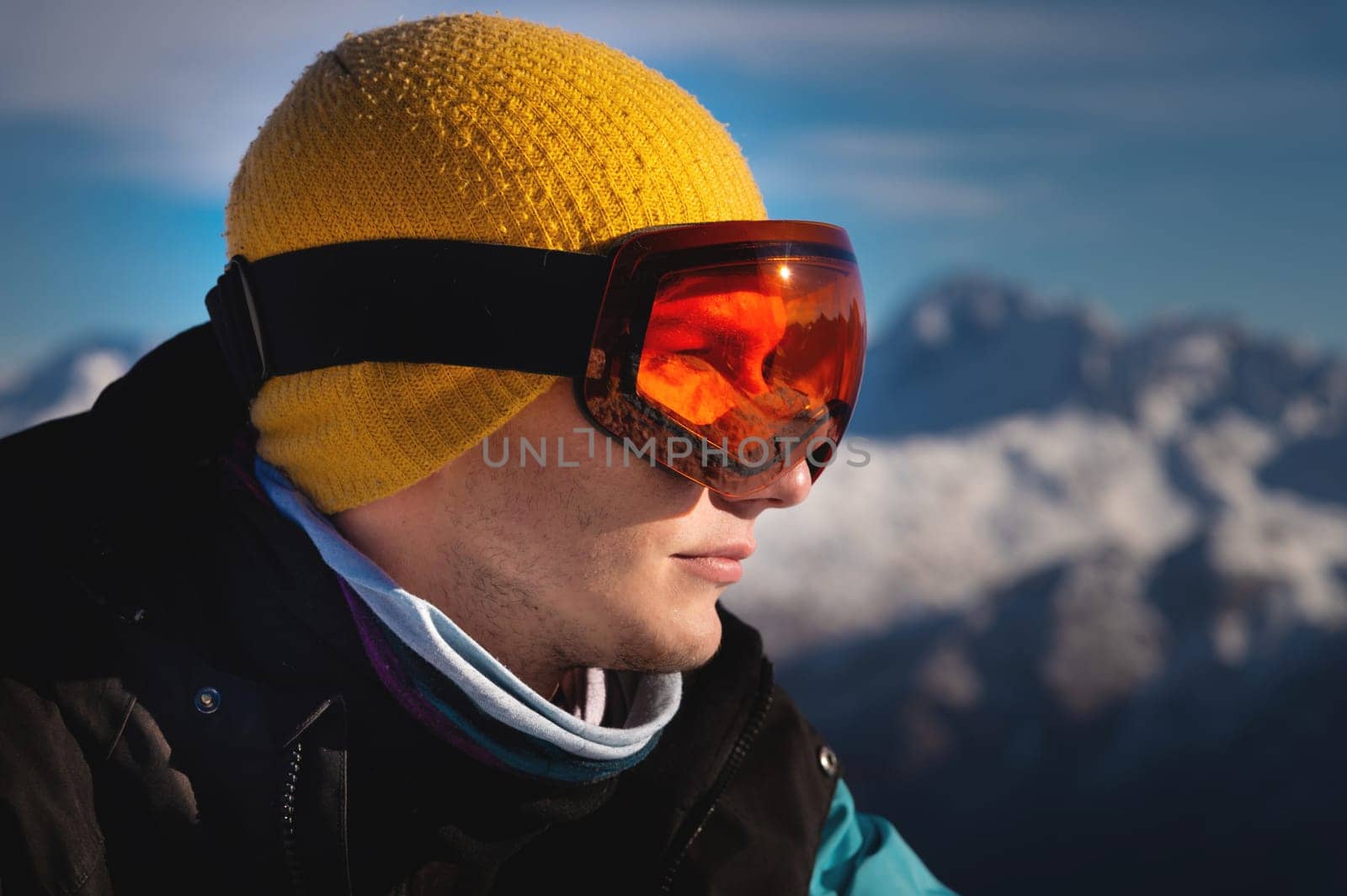 Male skier overlooking snow covered mountains on a sunny day, sun beams reflection in ski goggles by yanik88