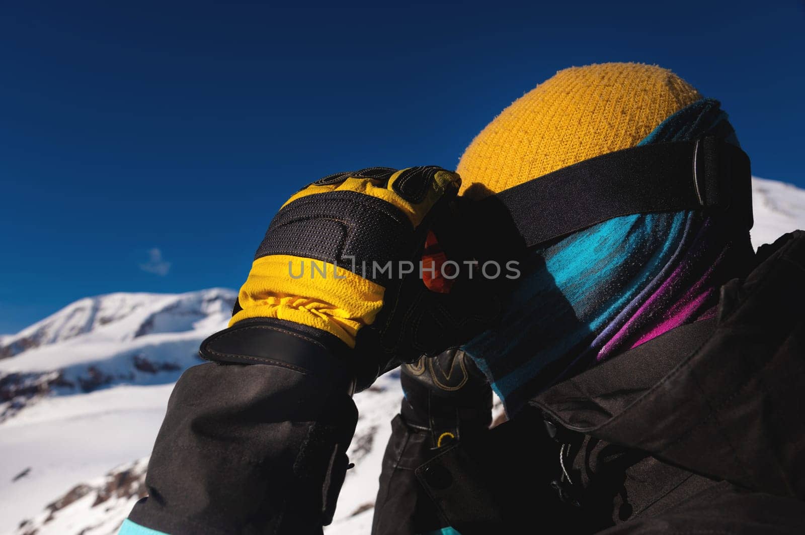 man in stylish sportswear and ski goggles. close up photo side view. a skier or snowboarder adjusts his mask before a quick descent from the mountain.