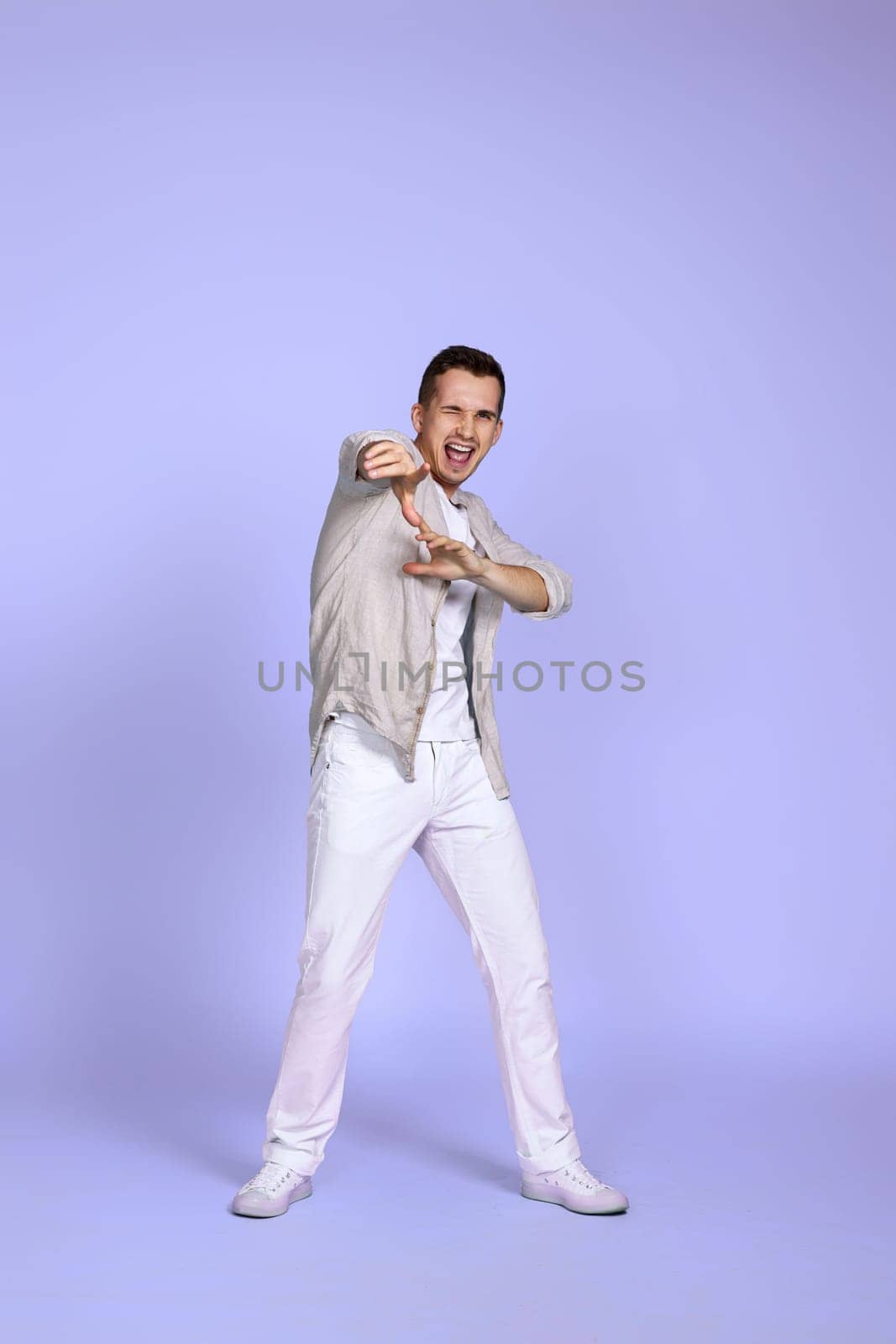optimistic caucasian young man pointing finger on camera on pastel violet background. Full body