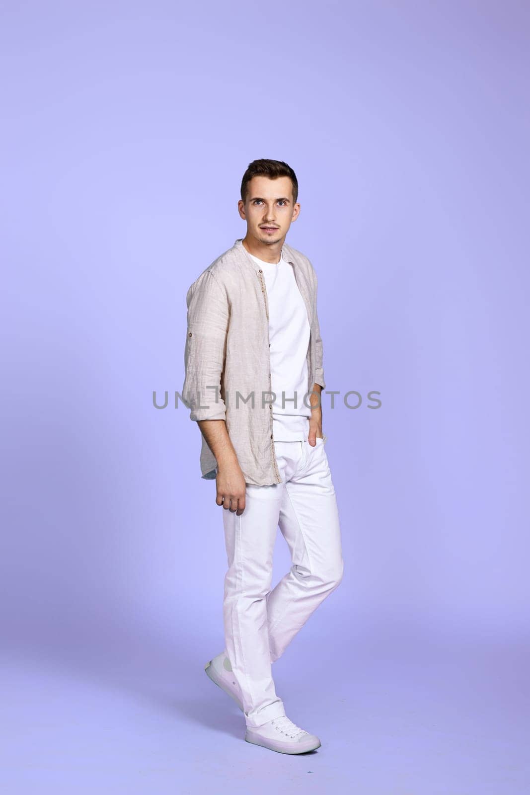 caucasian man in casual white clothes posing on pastel purple background. Full length photo