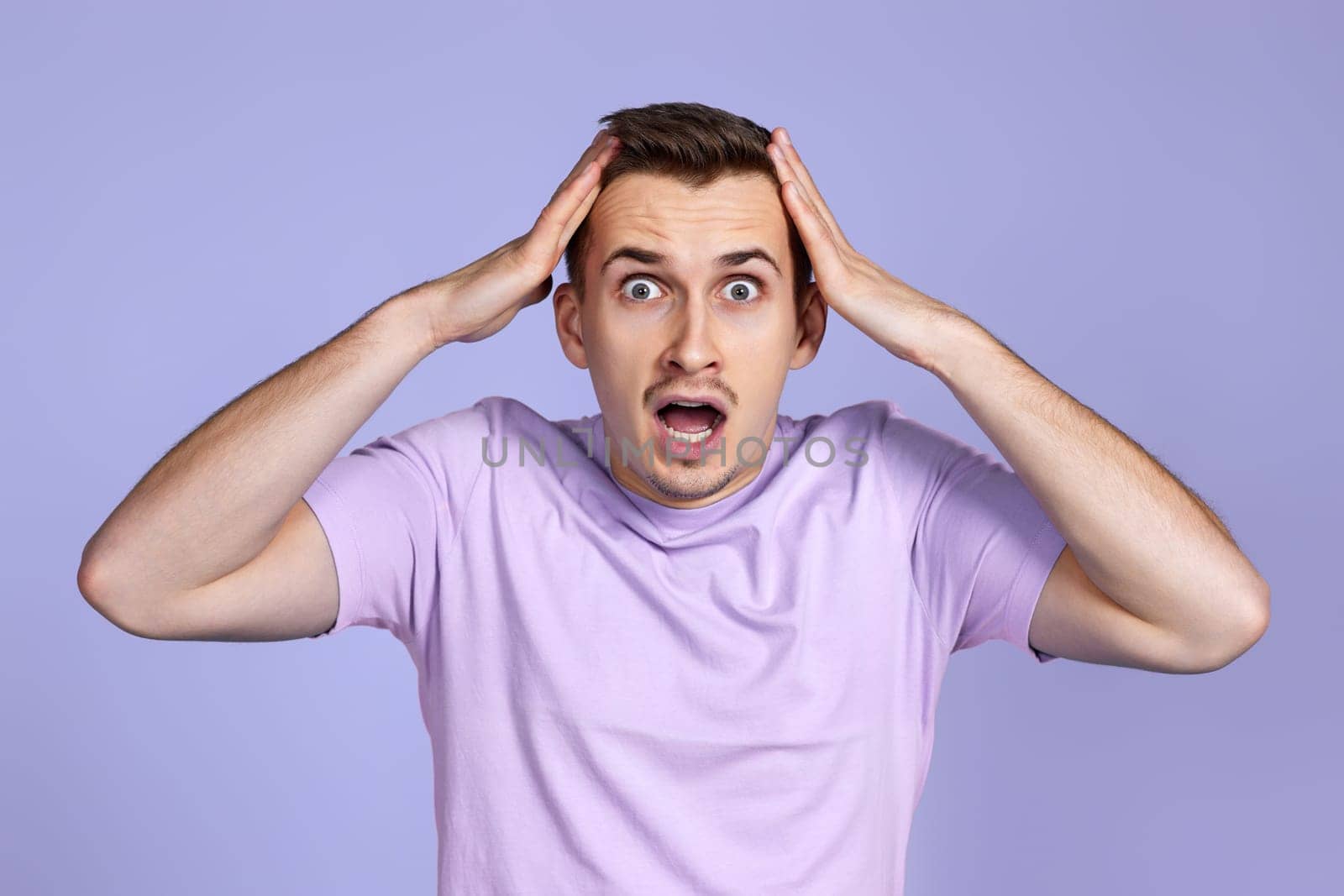 shocked man with surprise expression, fear and excited face on pastel purple studio background