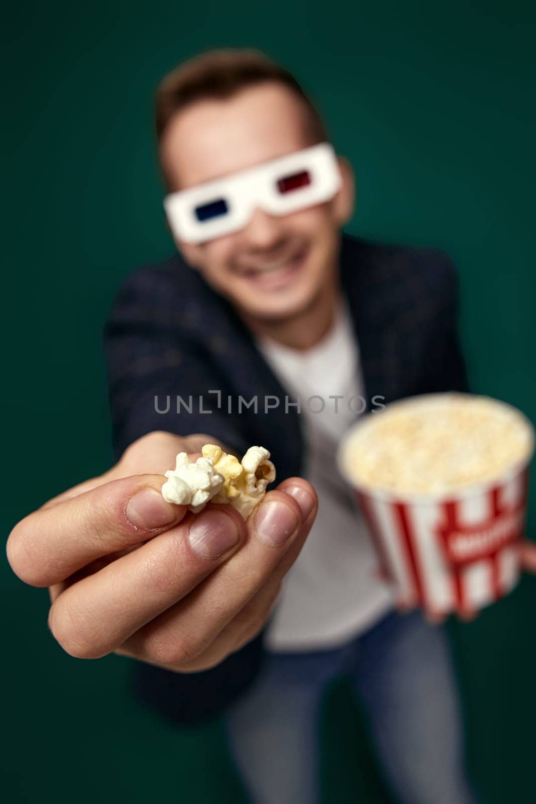 young man in 3d glasses showing popcorn on green background. focus on hand