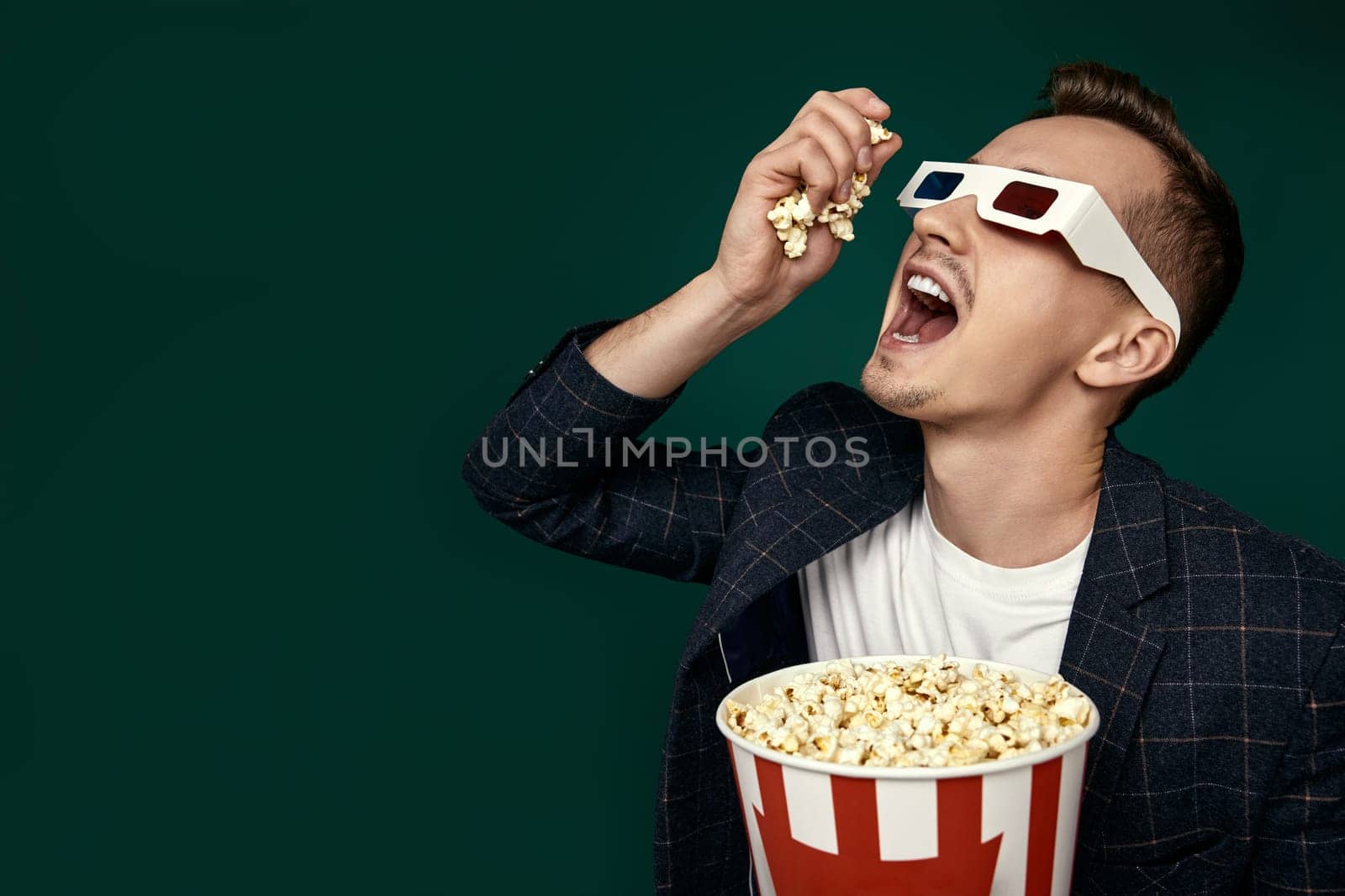 handsome man in 3d glasses and plaid jacket eating popcorn on green background. copy space