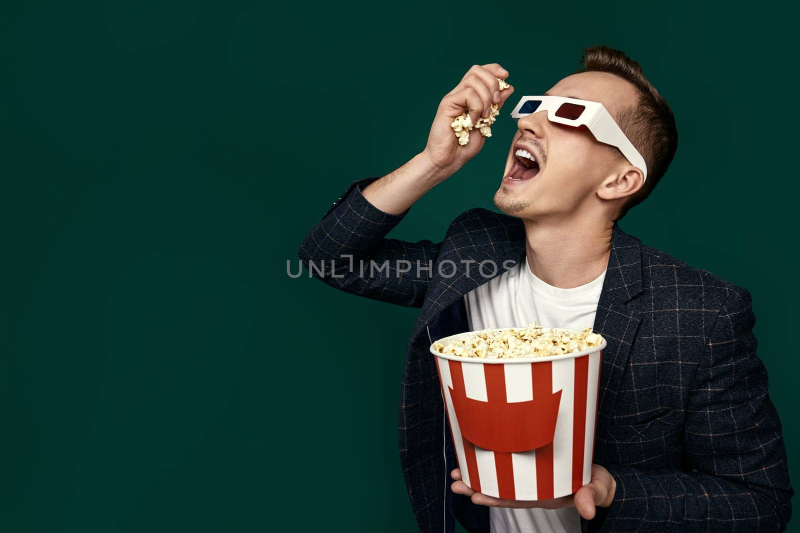 handsome man in 3d glasses and plaid jacket eating popcorn on green background. copy space