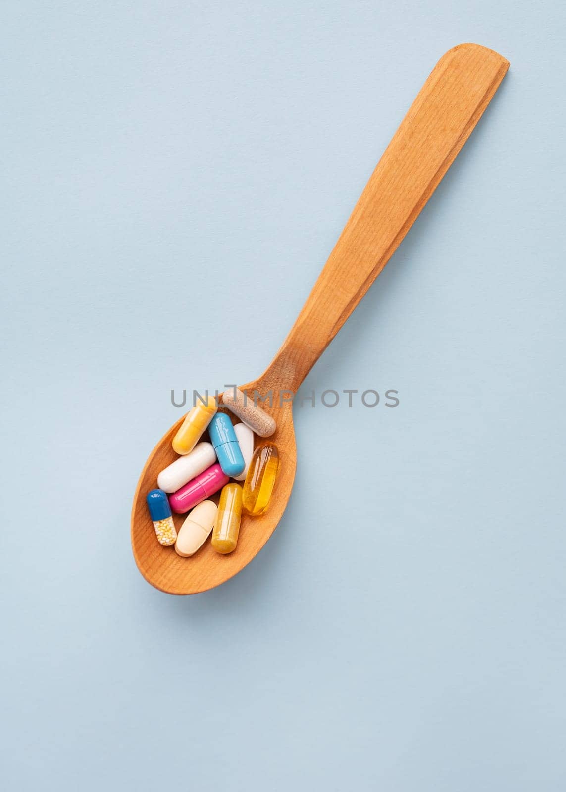 Various bright pills on a blue background lie in a wooden spoon. The concept of healthcare and evidence-based medicine, close-up. by sfinks
