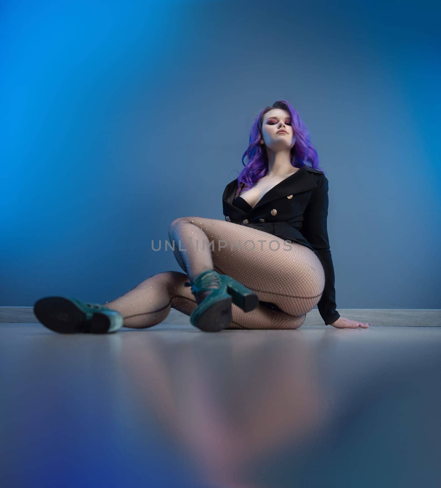 sexy girl in a fashionable jacket and with purple hair poses erotically in her underwear on a blue background of a copy paste