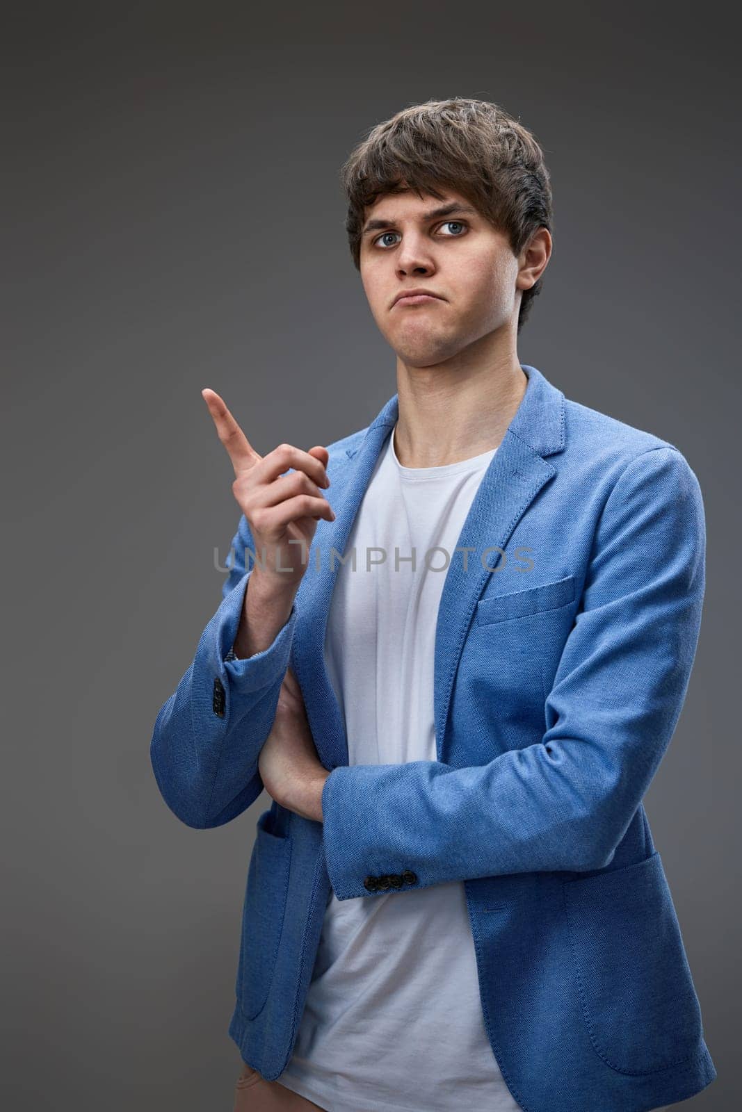 handsome caucasian young man in jacket pointing finger up on gray background