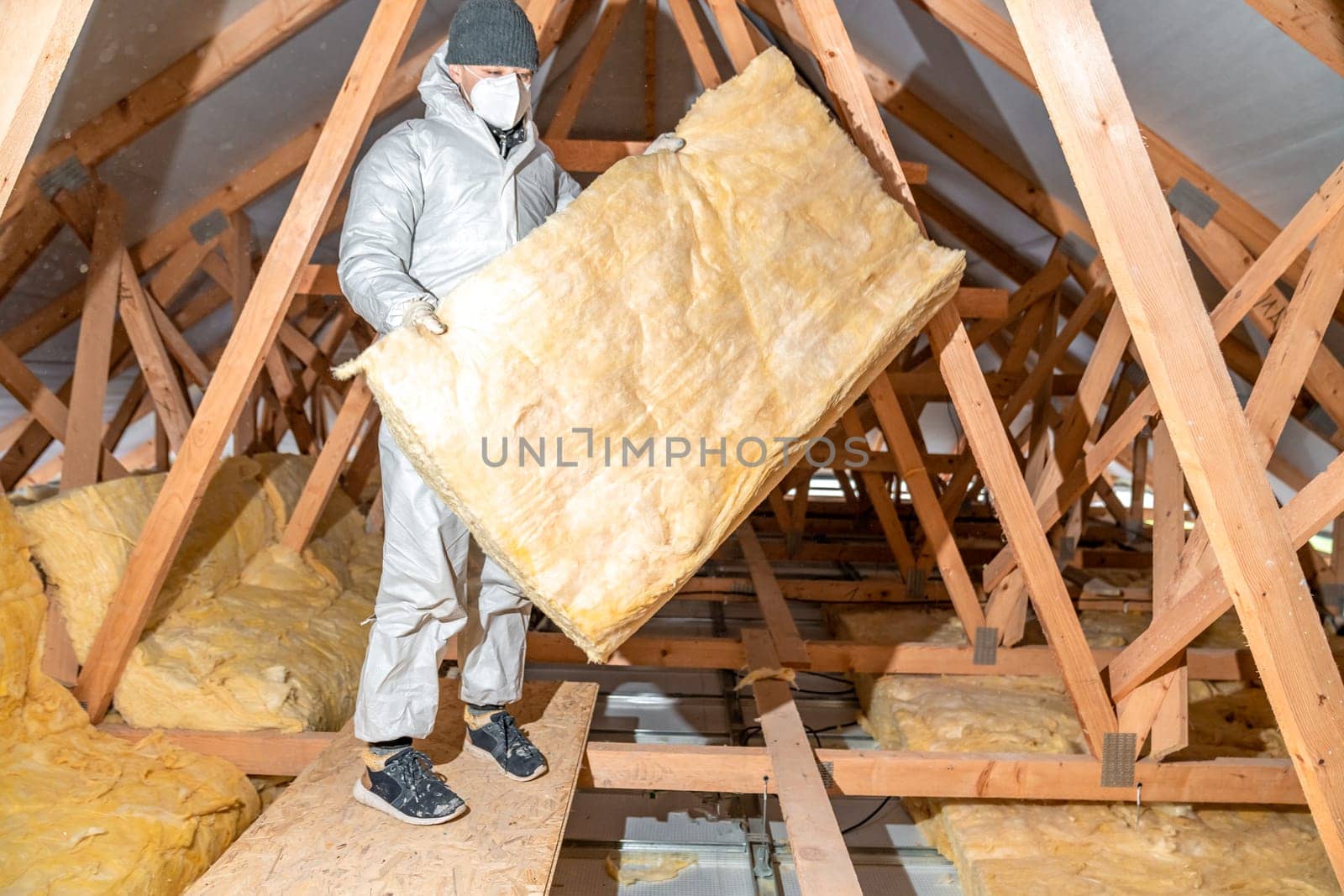 a worker in protective overalls works with glass wool by Edophoto
