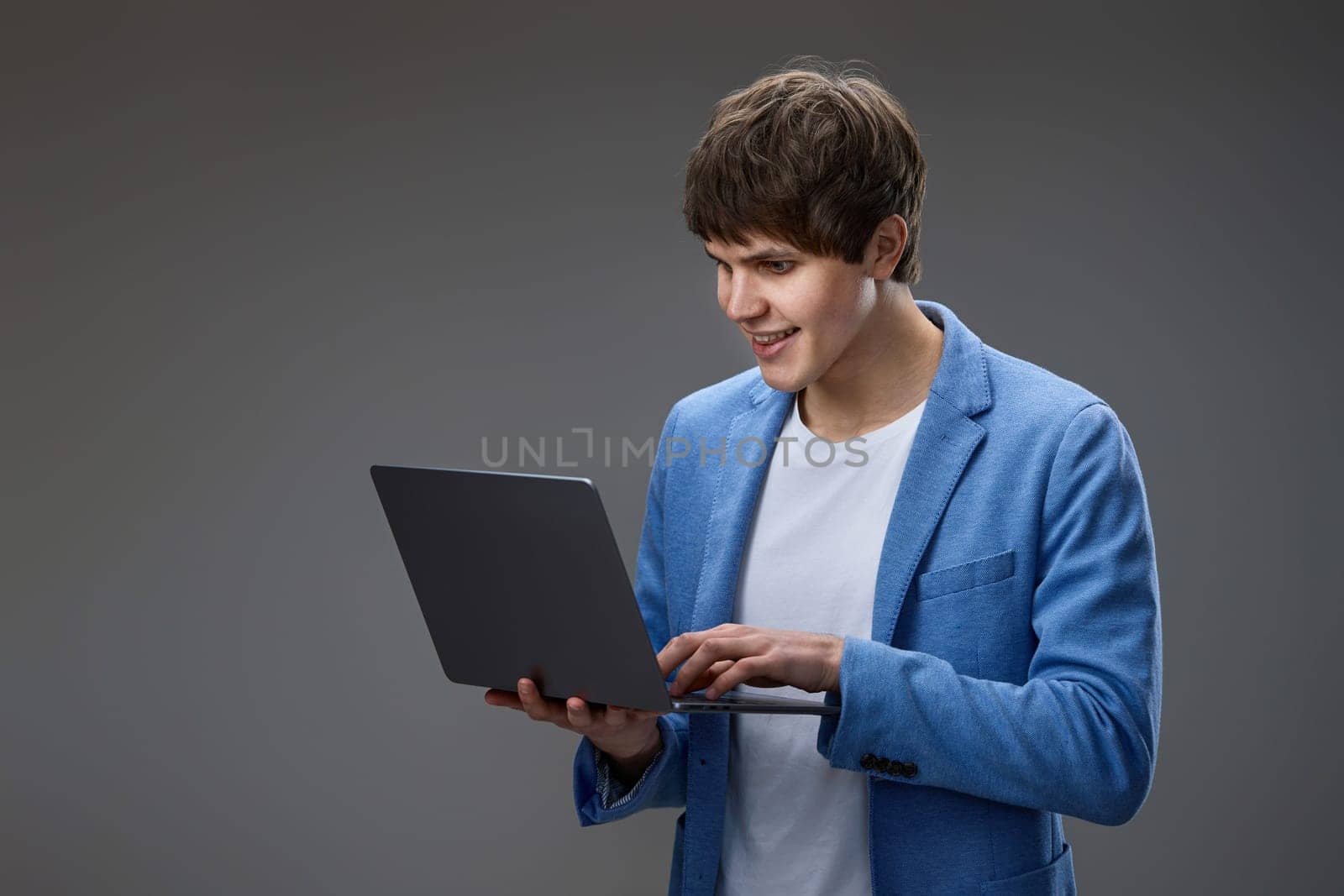 Cheerful caucasian man using laptop computer for online communication, typing messages isolated on gray background