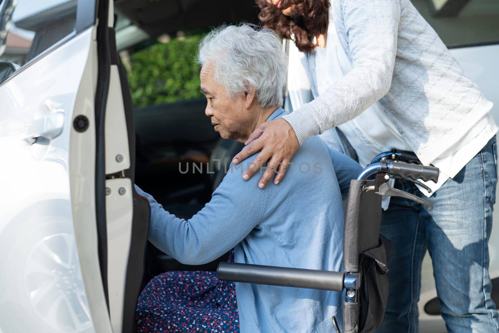 Caregiver help and support asian elderly woman sitting on wheelchair prepare get to her car to travel in holiday. by pamai