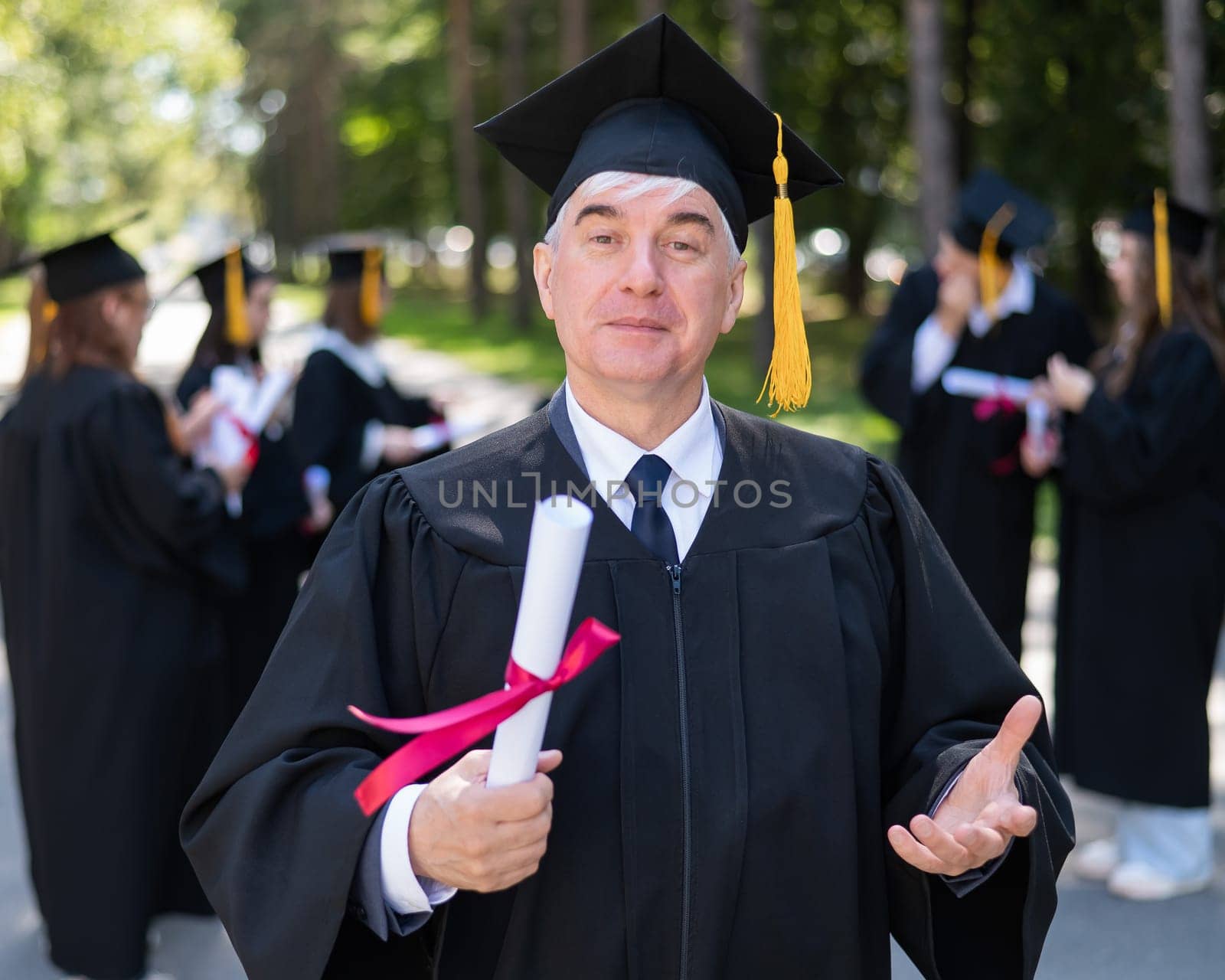 A group of graduates in robes outdoors. An elderly student rejoices at receiving a diploma. by mrwed54