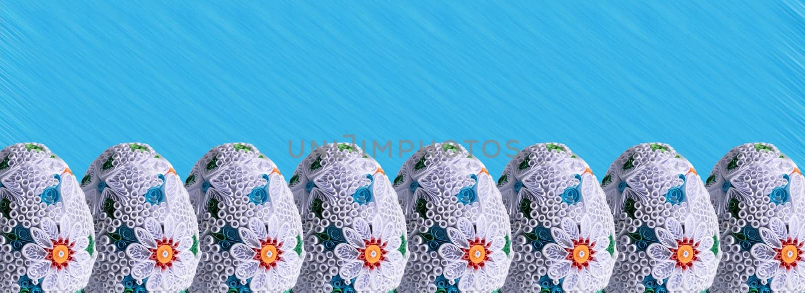 Many Easter eggs lined up one next to the other and the whole composition is set against a solid blue background.