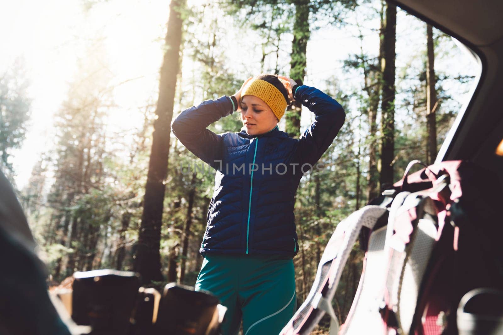 Woman putting on a headband at the trunk of the car, going on a hike by VisualProductions