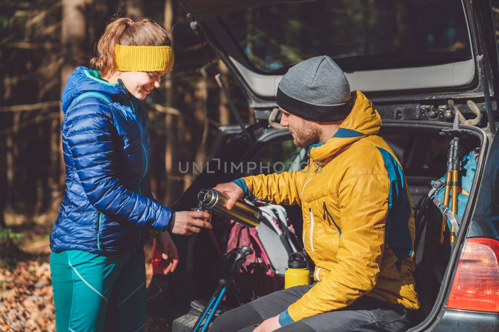 Couple of hikers drinking some tea form a thermo flask sitting in the car trunk by VisualProductions