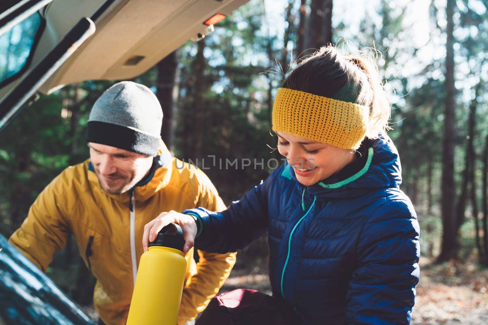 Smiling mountaineering couple packing their things into backpacks in the car trunk by VisualProductions