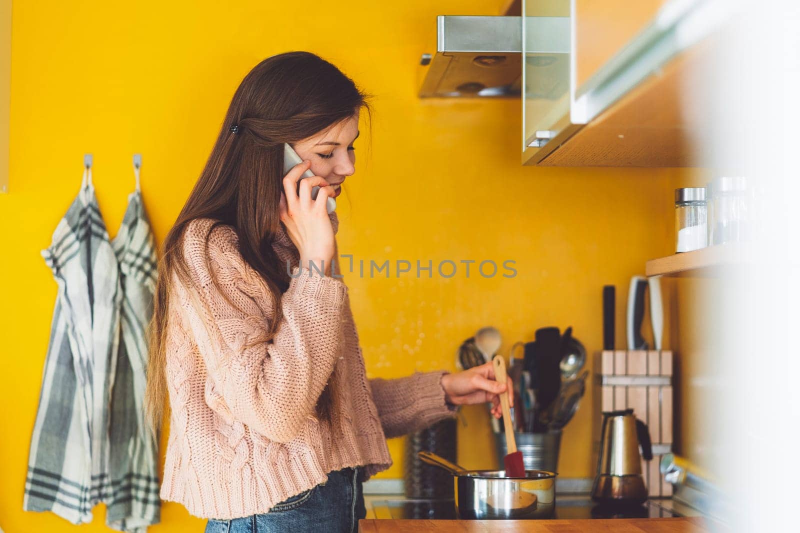 Young woman cooking lunch at home while talking on the phone for work by VisualProductions