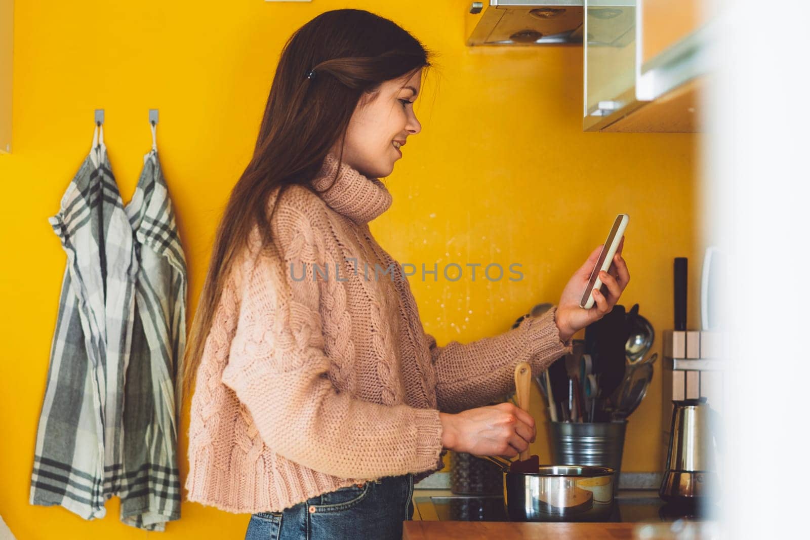 Side view of a woman in her kitchen making lunch while talking on a video call for work by VisualProductions