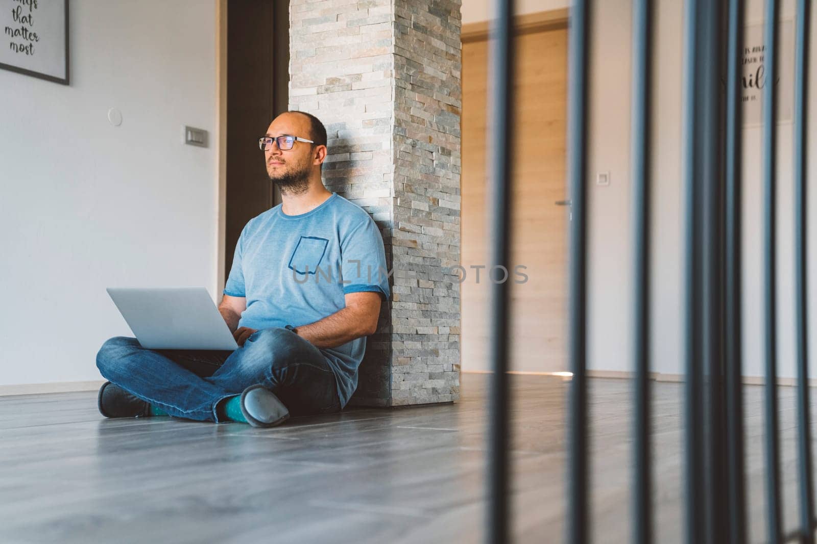 Man sitting with his legs crossed on the floor with laptop on his lap working by VisualProductions