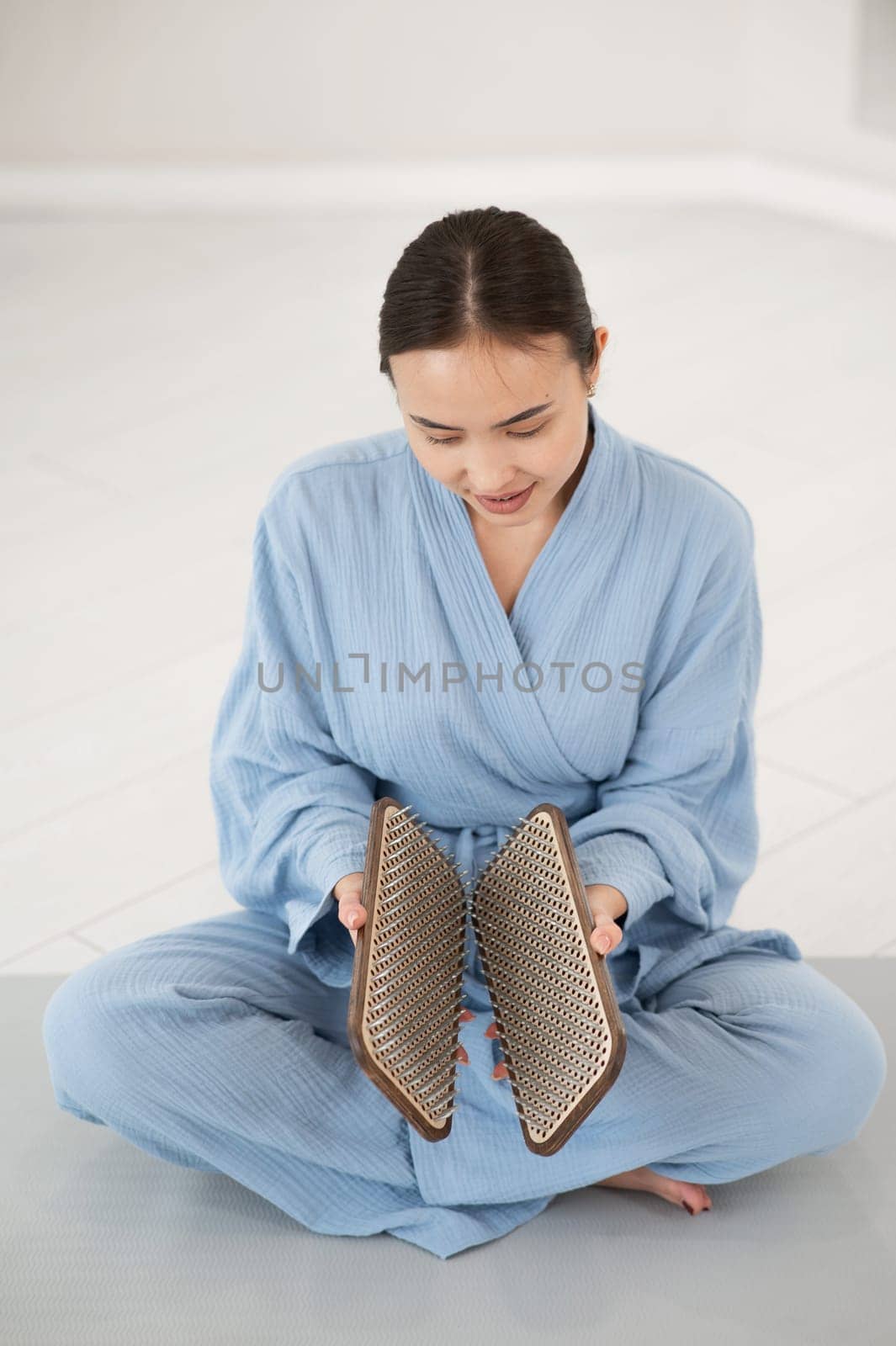 Asian woman sitting in lotus position on yoga mat and holding sadhu boards. by mrwed54