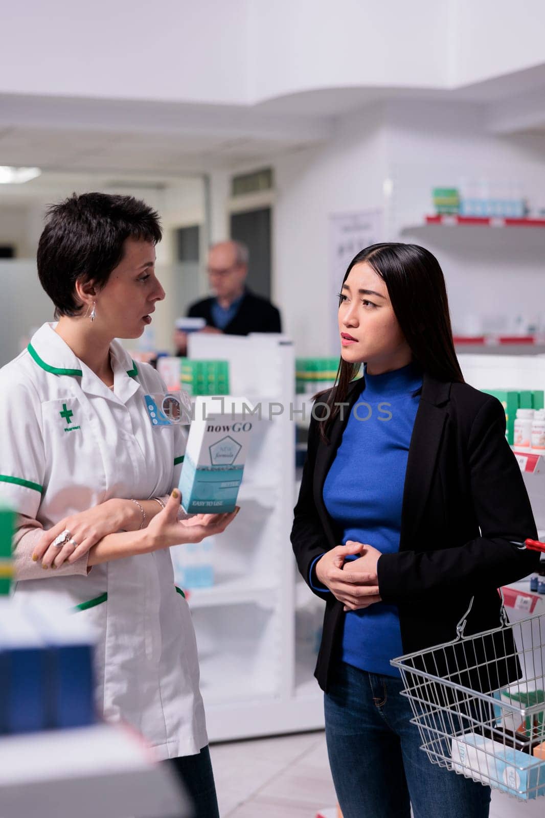 Drugstore worker giving customer assistance in choosing food poisoning remedy. Young asian woman holding hand on stomach and explaining abdominal pain symptom to pharmacy employee