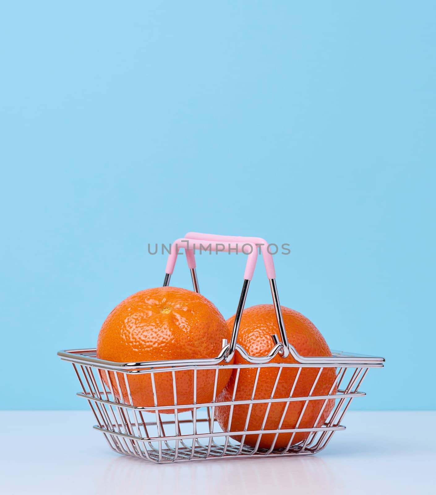 Ripe mandarins in a miniature metal shopping cart on a blue background, citrus price increase concept