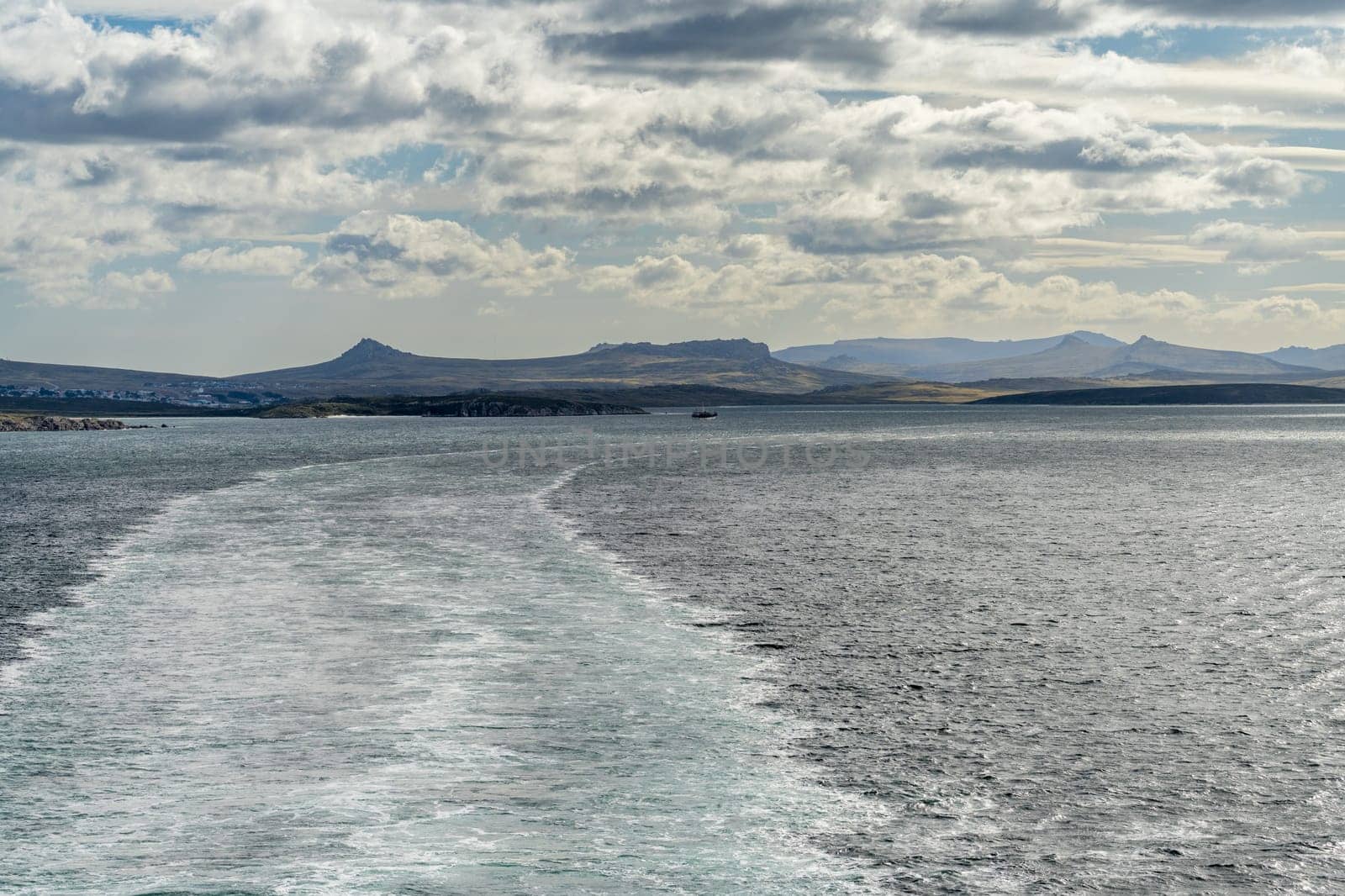 Rugged headlands and rocks as cruise ship departs from port of Stanley on the Falkland Islands
