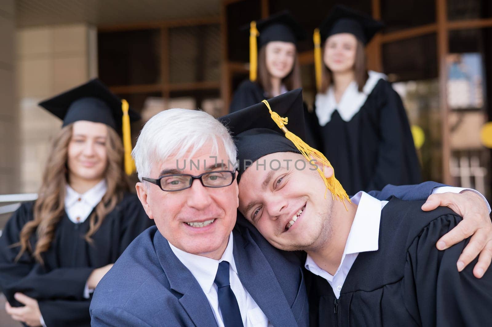 Father and son embrace at graduation. Parent congratulates university graduate